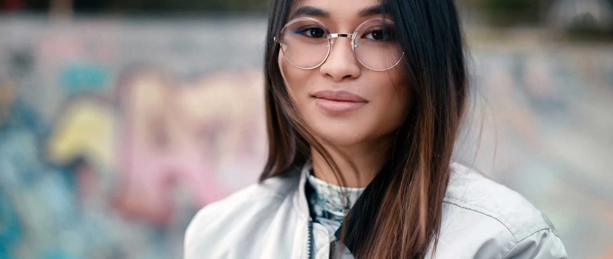 Mulher usando uma armação metálica com lentes incolores em um ambiente urbano.