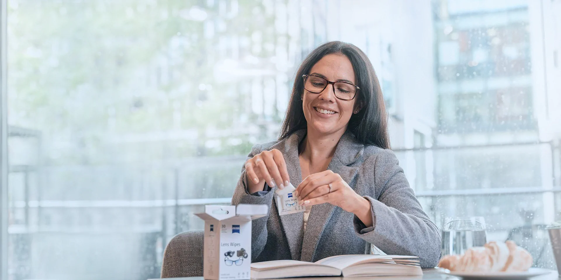 Mulher abre um lenço ZEISS para lentes em um café.