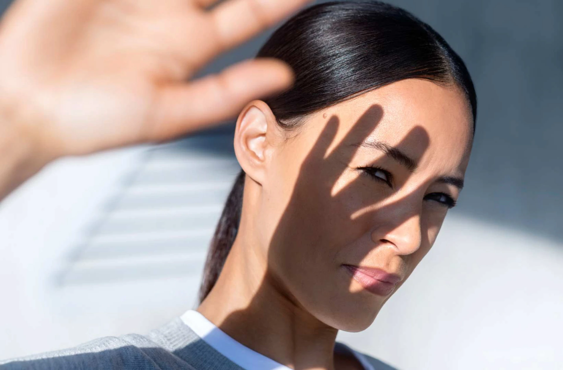 Uma mulher protege o rosto da luz do sol com a mão.